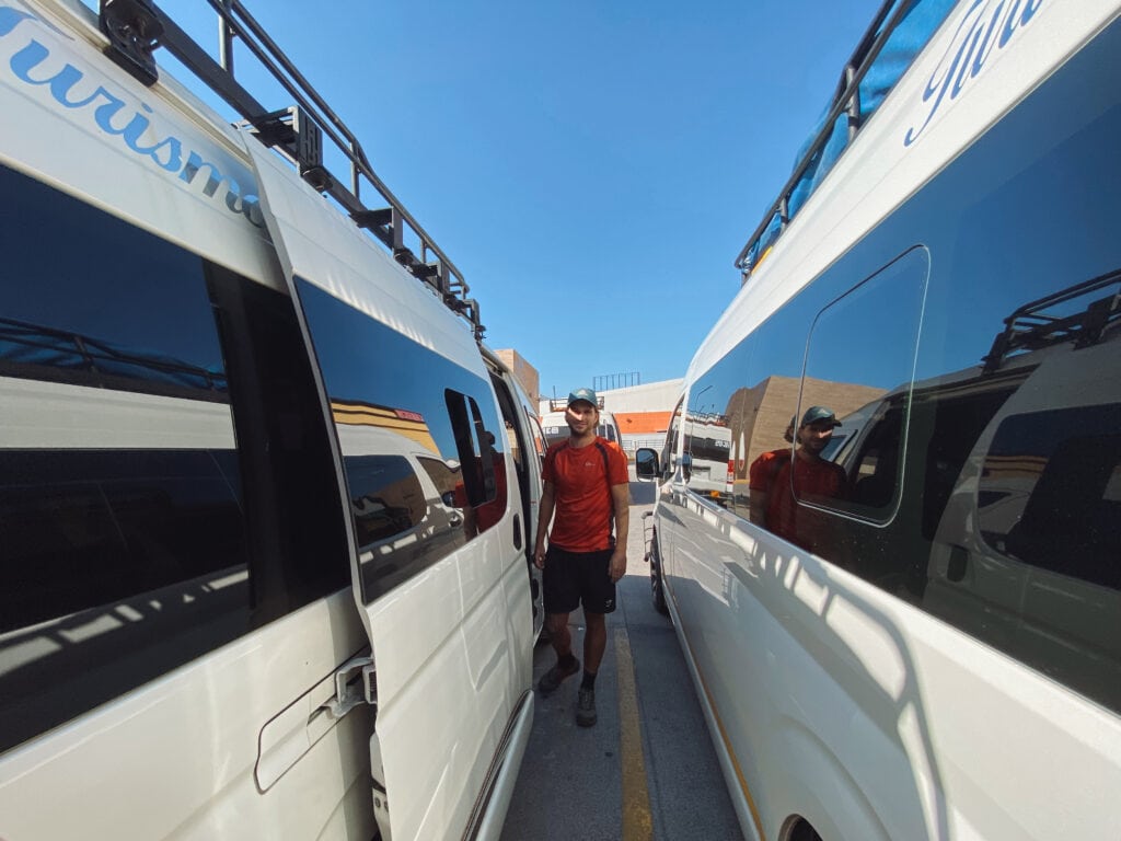 Dan in a red shirt standing between two white shuttle buses.