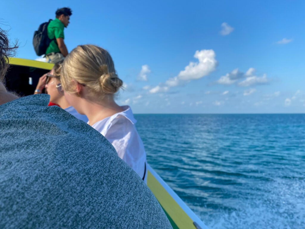 People sitting on a boat and blue water to the right hand side of the frame.