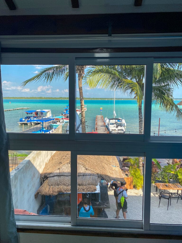 A view out a window of a very blu lake with a dock with a sail boat.