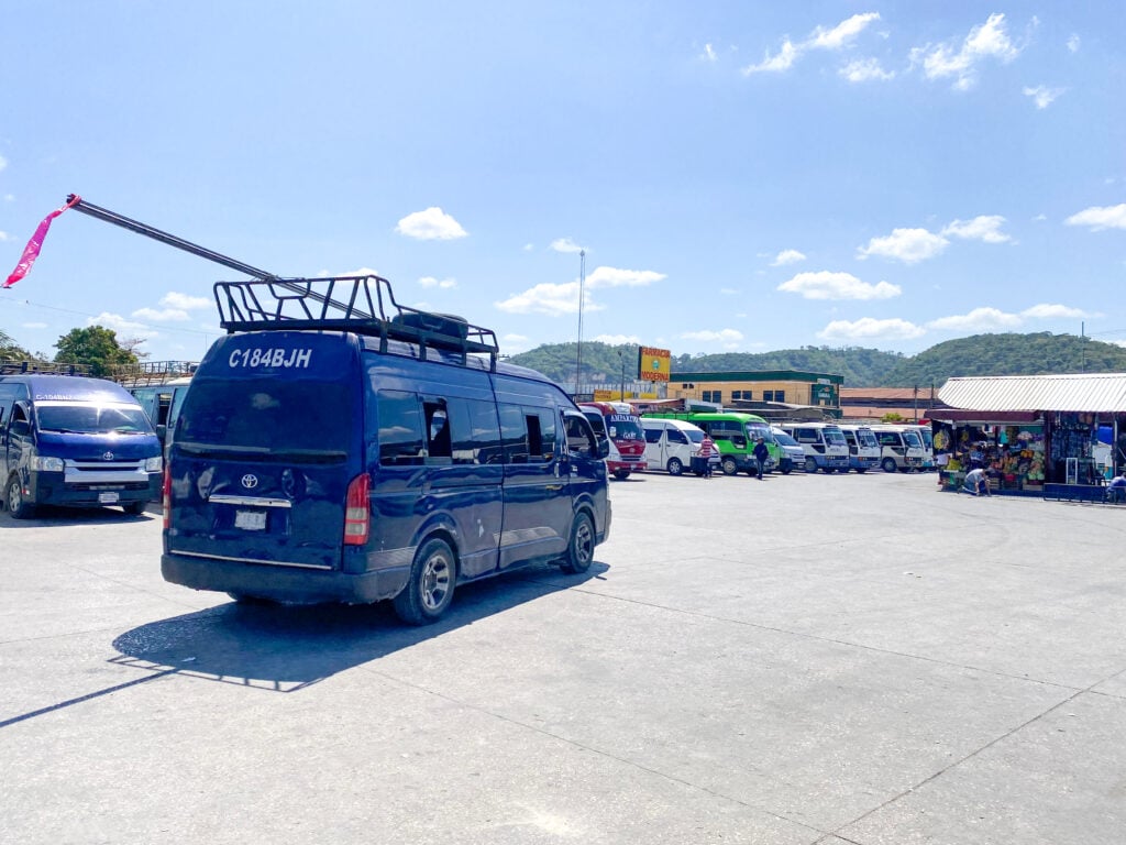 A black van in the foreground of a large parking lot with many other vans.