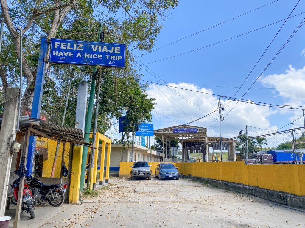 A blue sign that says "feliz viaje have a nice trip" at the Guatemala Belize border.