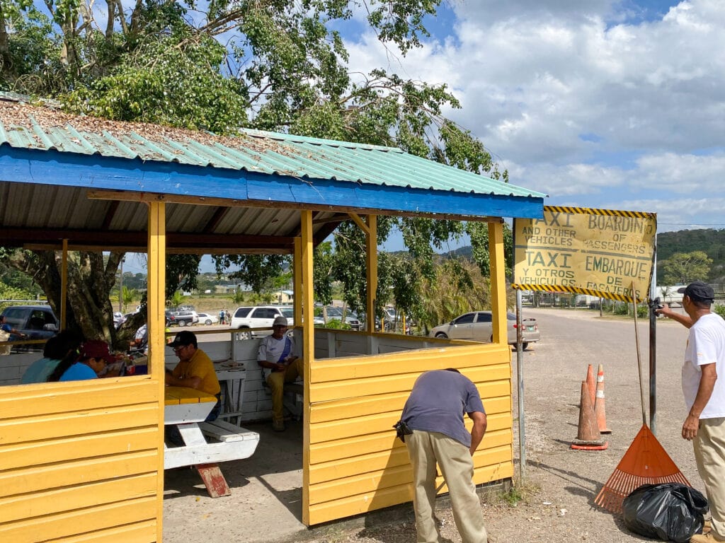 A yellow painted shack with green tin roof and sign next to it that says "taxi boarding".