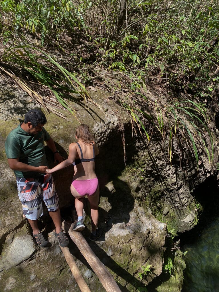 William helps Sarah across the two sticks that connect one side of the canyon to the other.