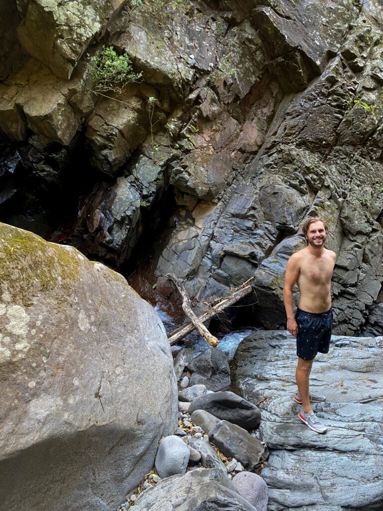 Dan stands on a boulder wearing Tropicfeel shoes and swim trunks and smiles at the camera.