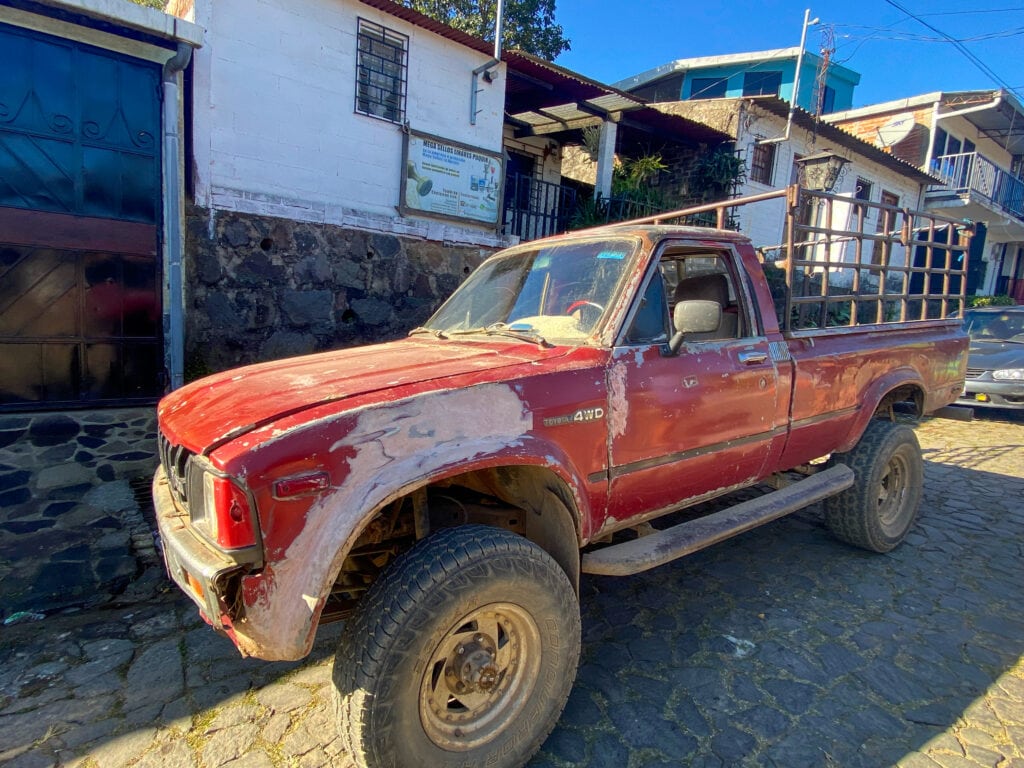 A rusty red pickup truck on a cobbled street in Ataco, El Salvador for the pickup for the cliff jumping in El Salvador tour.