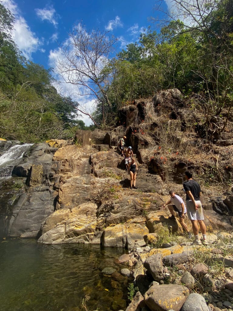 A group of travelers hike down some rocks next to a waterfall.