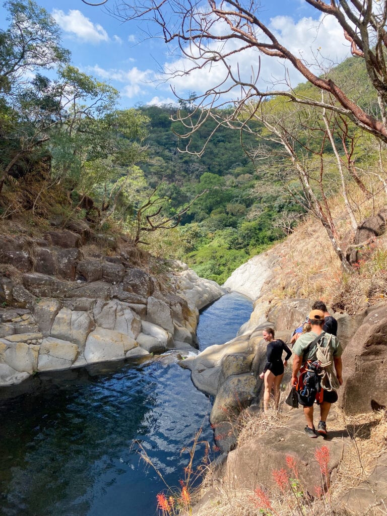 A group of people hike beside a rocky river.