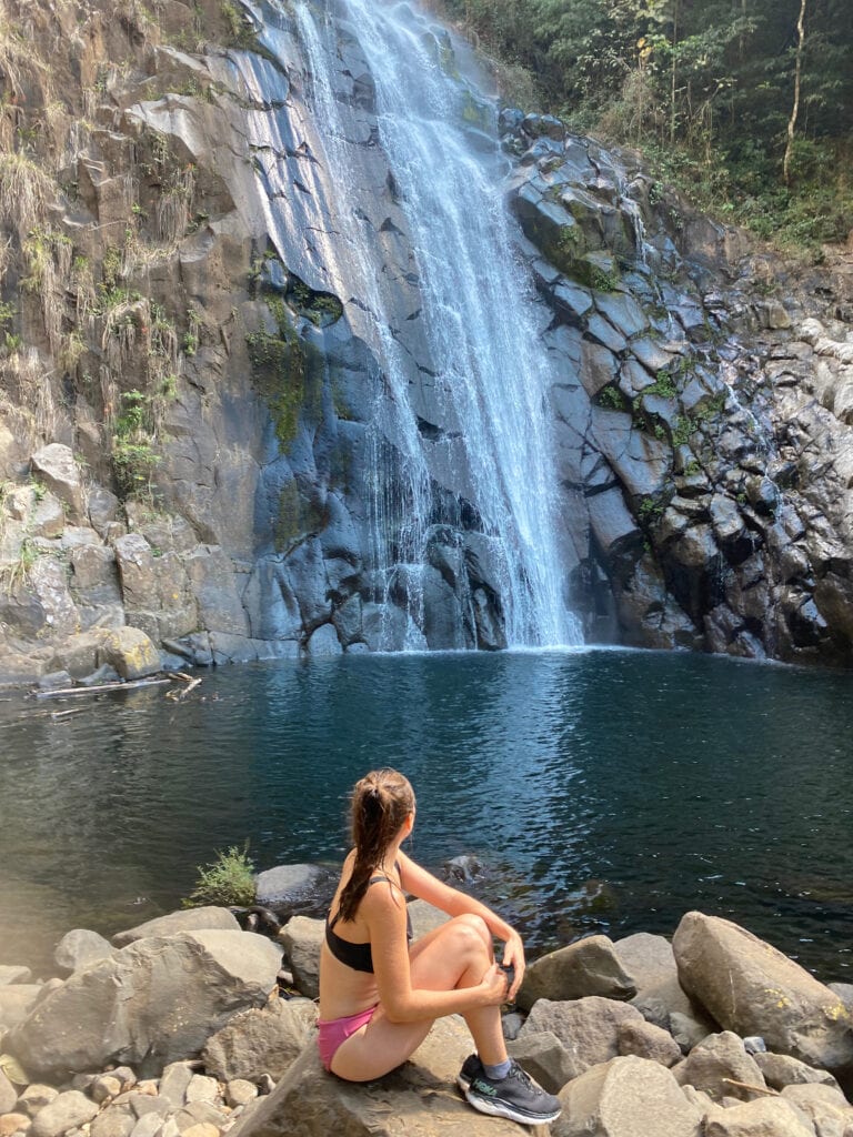 Sarah sits at the base of Cascada el Perol, a waterfall in El Salvador, after cliff jumping in El Salvador with El Salvatours.