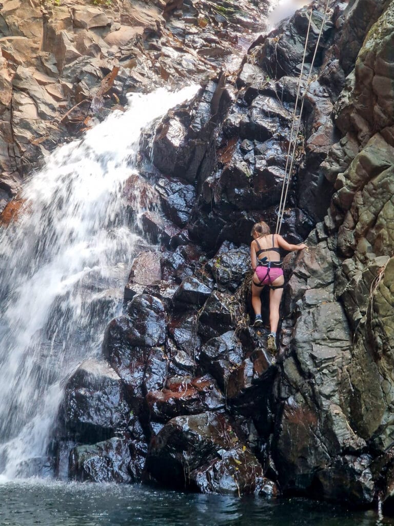 Sarah rock climbing down a cliff face next to a waterfall.