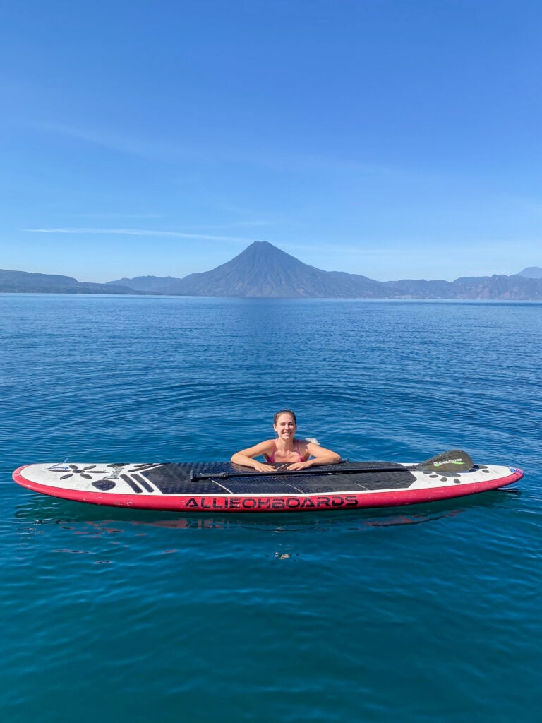 Sarah swimming in Lake Atitlan, leans on paddle board and smiles for camera.