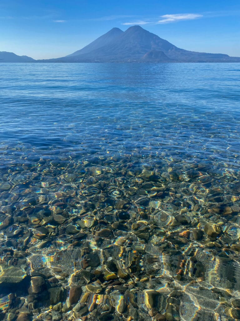 Clean blue waters of Lake Atitlan with a volcano in the distance.