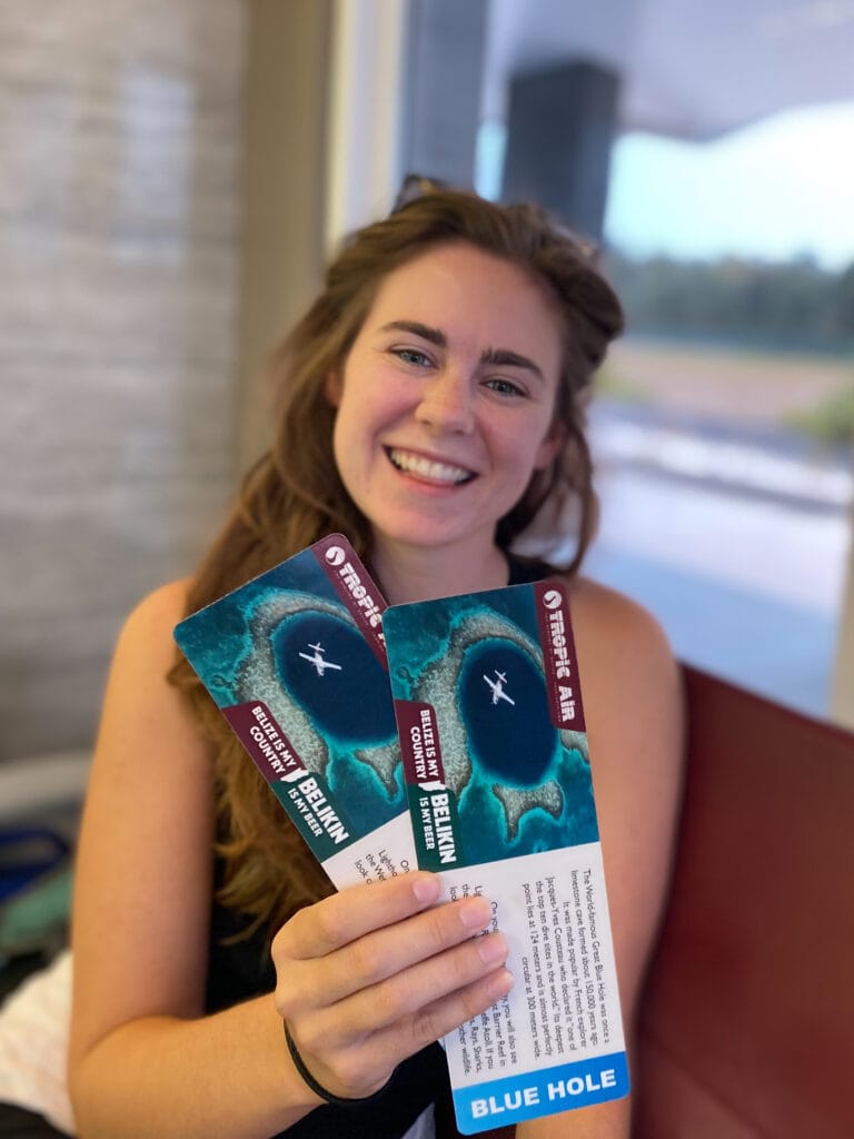 Sarah smiles holding two Blue Hole flight tickets