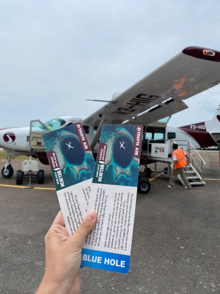 Two tickets for Tropic Air flight to Blue Hole in Belize, held up in front of small 11 person plane.