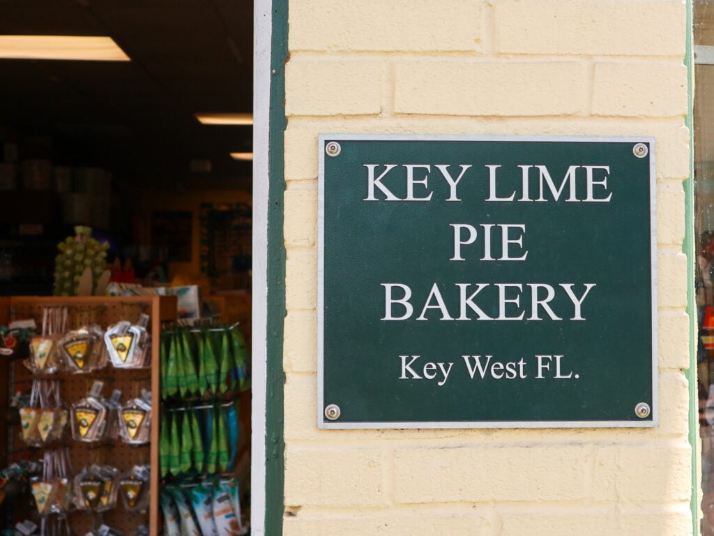 A green sign on yellow brick wall that reads key lime pie bakery key west FL.