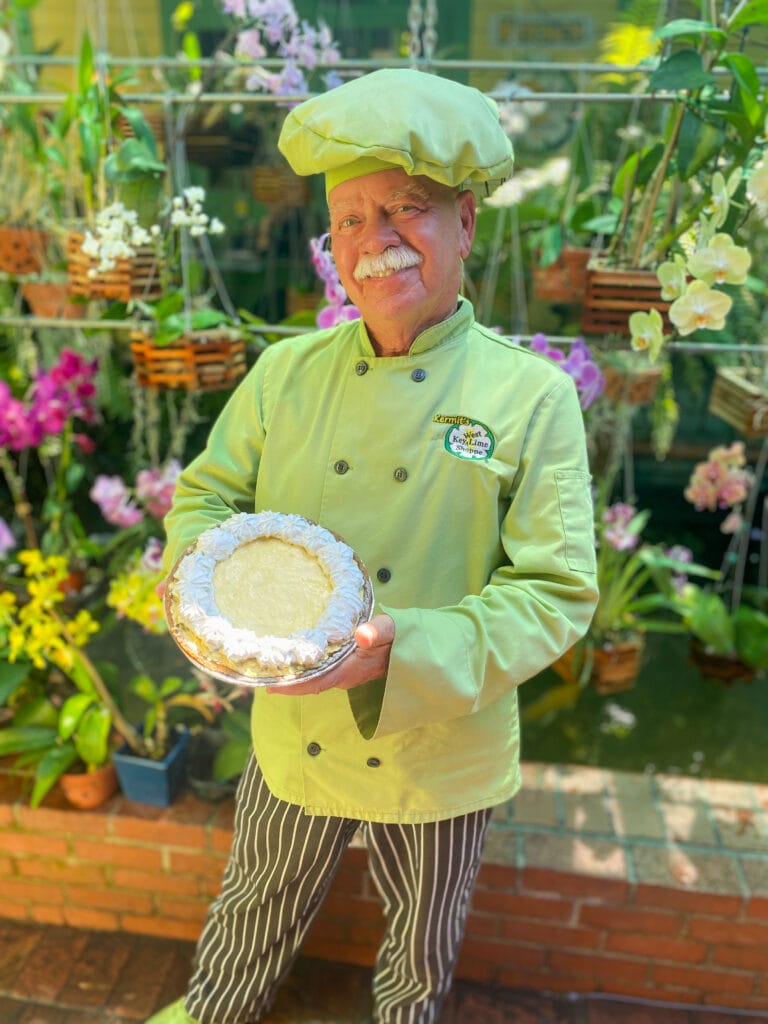 Kermit, the owner of Kermit's key west key lime pie shop, wears a lime green chef outfit and holds a gluten free key lime pie in key west location.