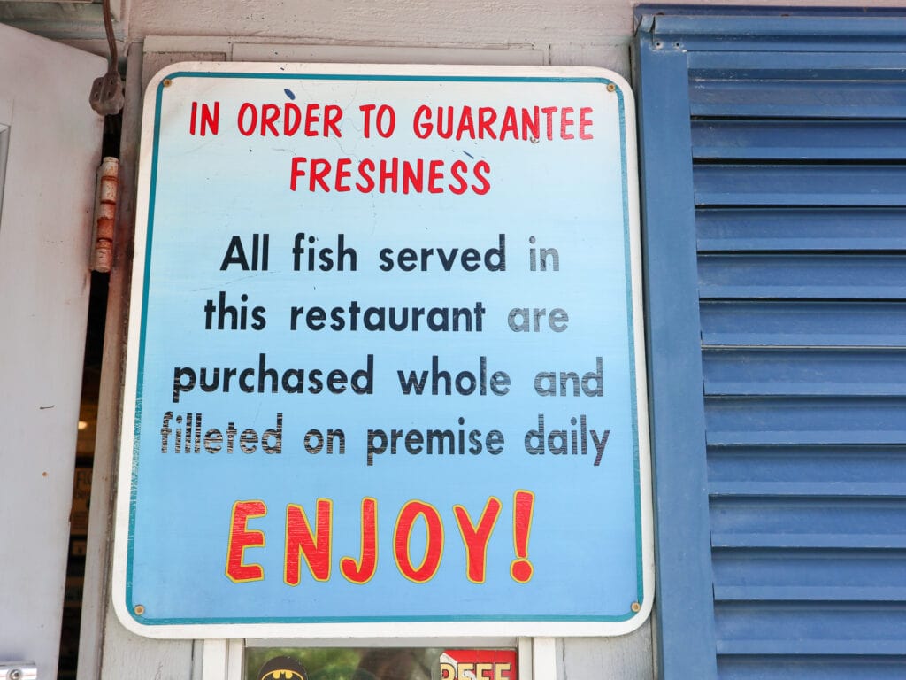 A blue sign reads "in order to guarantee freshness all fish served in this restaurant are purchased whole and pilleted on premise daily".