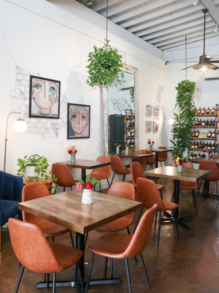 A white interior of a cafe with four brown tables and handing houseplants.