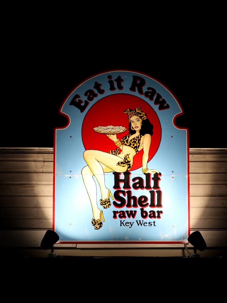 A sign that reads "eat it raw, half shell raw bar key west". Raw bar is a gluten free key west restaurant.