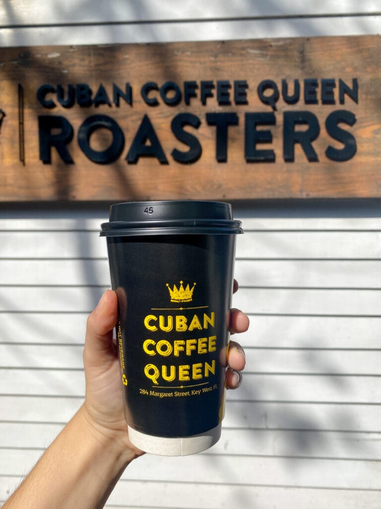 Sarah's hand holding a black coffee cup that reads "cuban coffee queen".