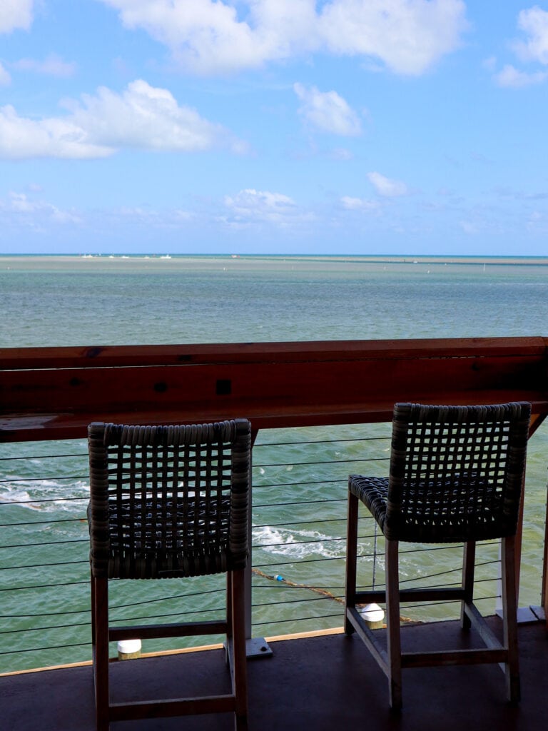Two bar chairs look out at an expansive ocean.