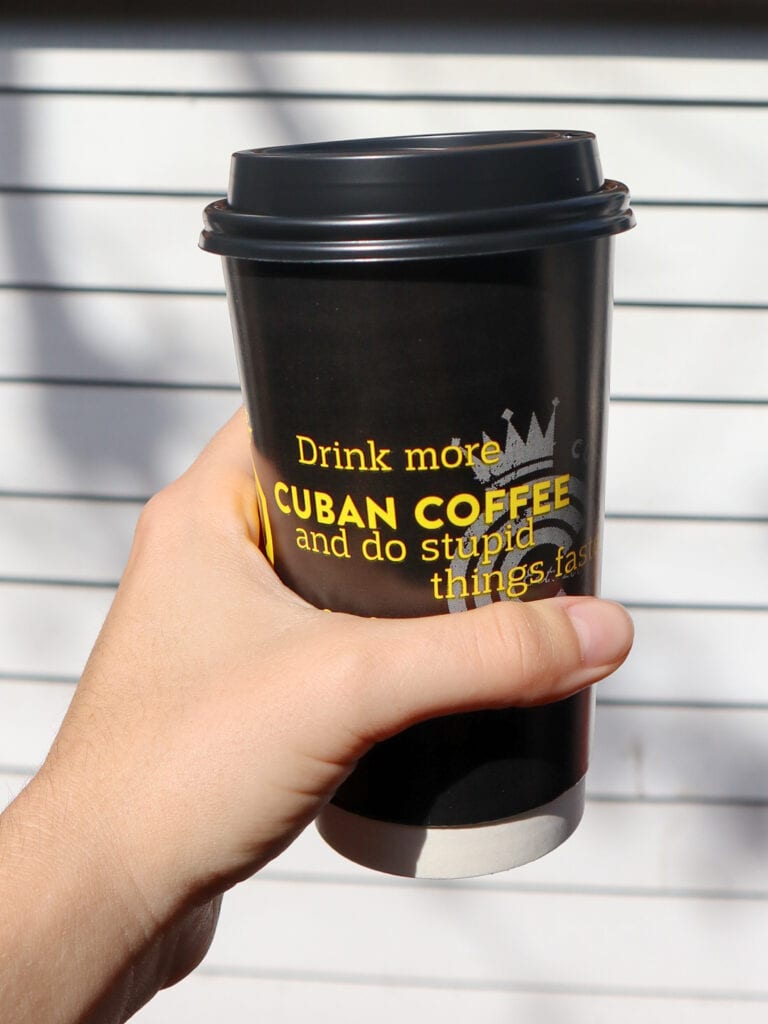 A black takeout coffee cup that reads "drink more cuban coffee and do stupid things faster"
