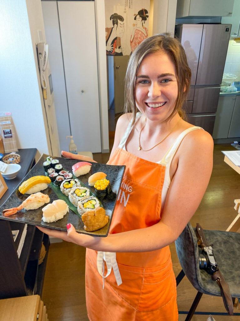 Sarah smiles and holds her sushi.