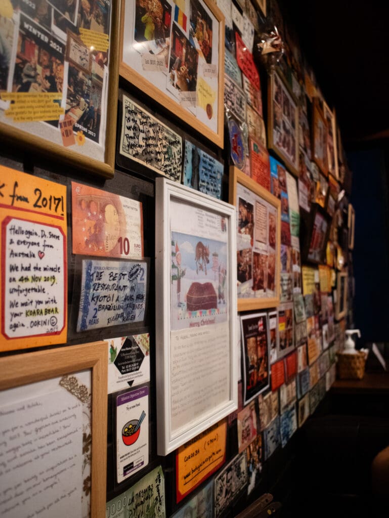 Wall of Kyoto restaurant covered in cards signs and money.