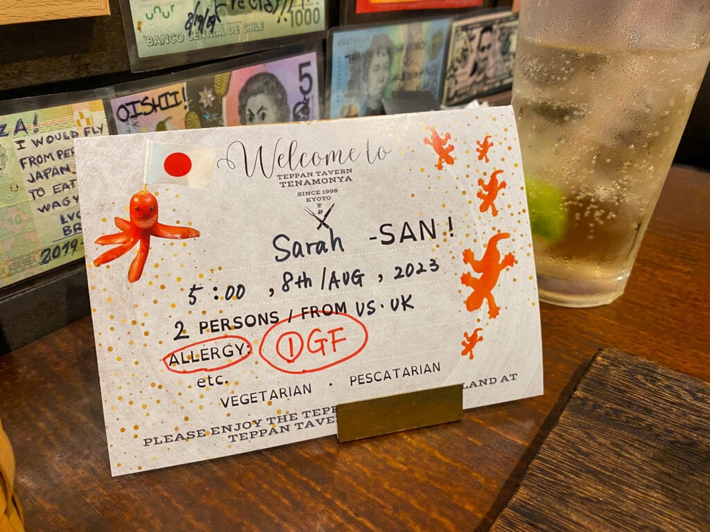 Paper sign that says Welcome to teppan tavern tenamonya Kyoto Sarah - San and notes allergy GF.