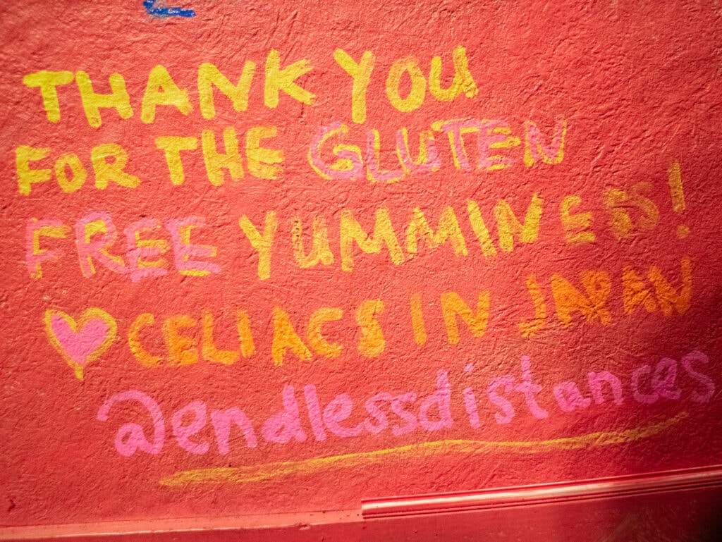 Yellow writing on red wall that reads "thank you for the gluten free yumminess! Heart celiacs in Japan @endlessdistances"