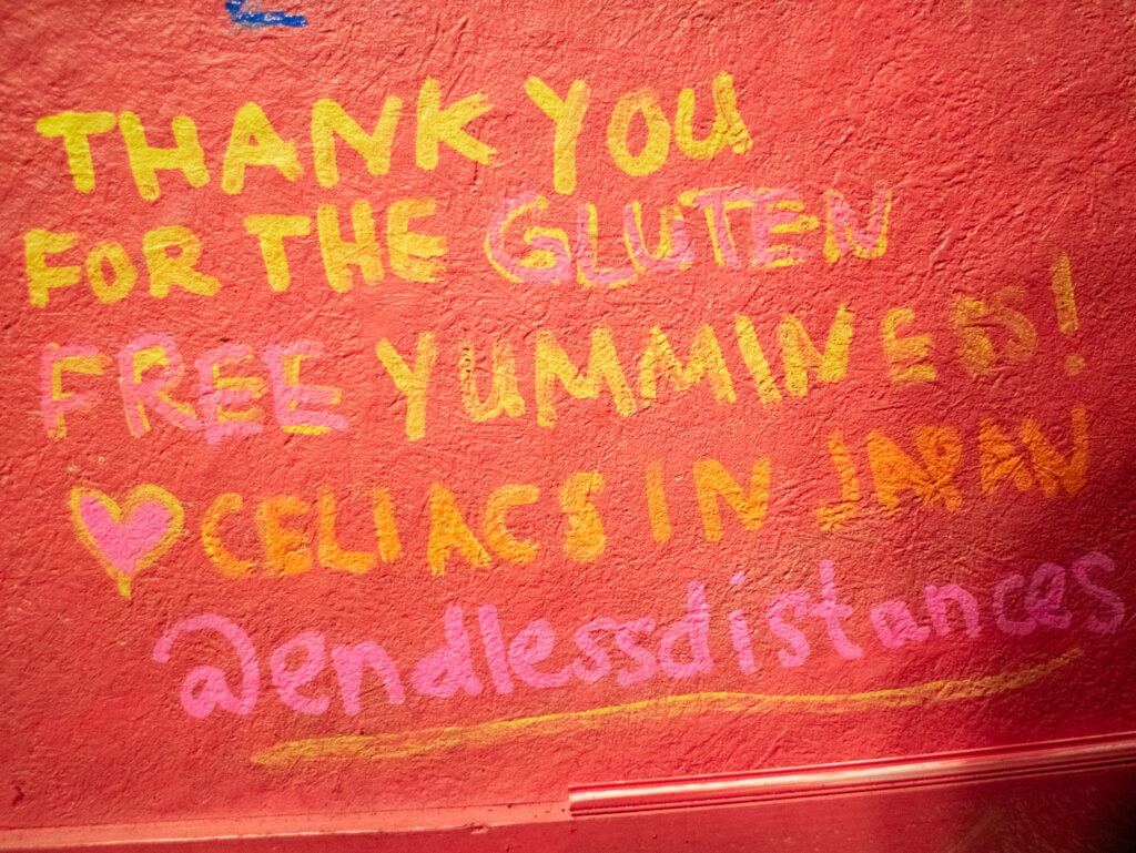 Yellow writing on red wall that reads "thank you for the gluten free yumminess! Heart celiacs in Japan @endlessdistances"