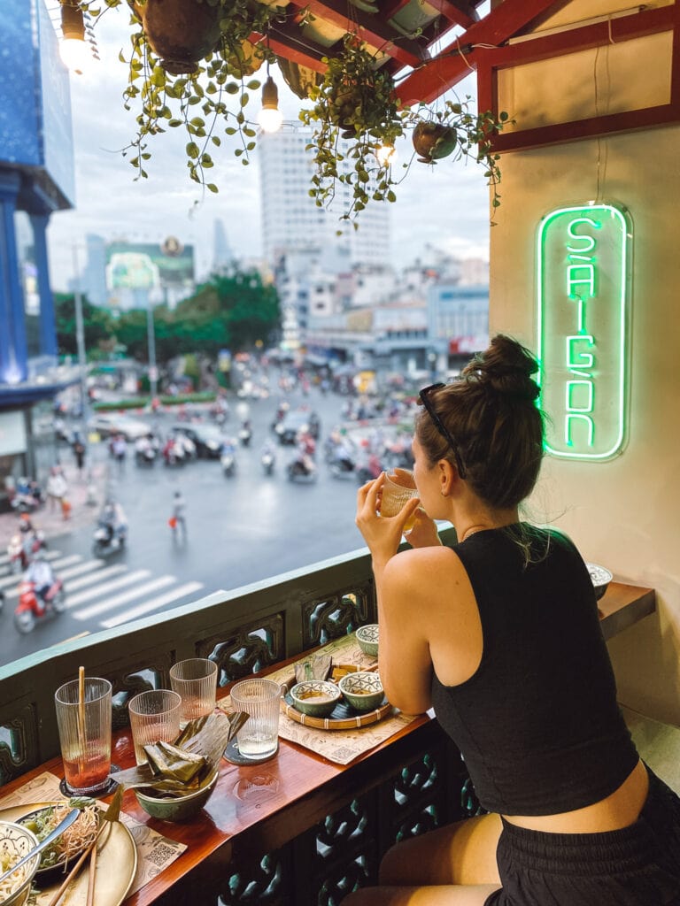 Sarah sitting on balcony of O Tinh House restaurant in Ho Chi Minh, overlooking traffic with neon sign that says Saigon