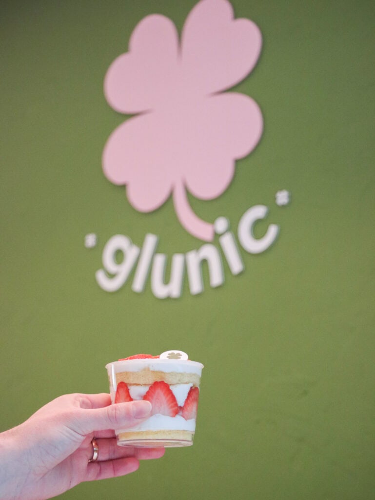 Hand holding cup of gluten free strawberry cake, wall says "glunic" in background.