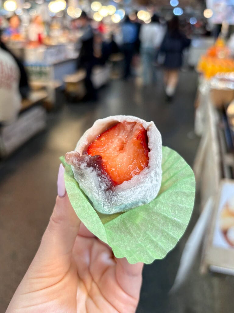 hand holding strawberry mochi with a bite taken out.