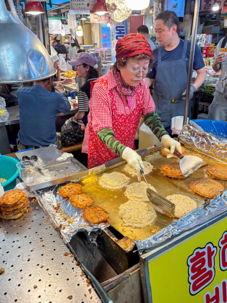 Korean woman cooking mung bean pancakes at Gwangjang Market.