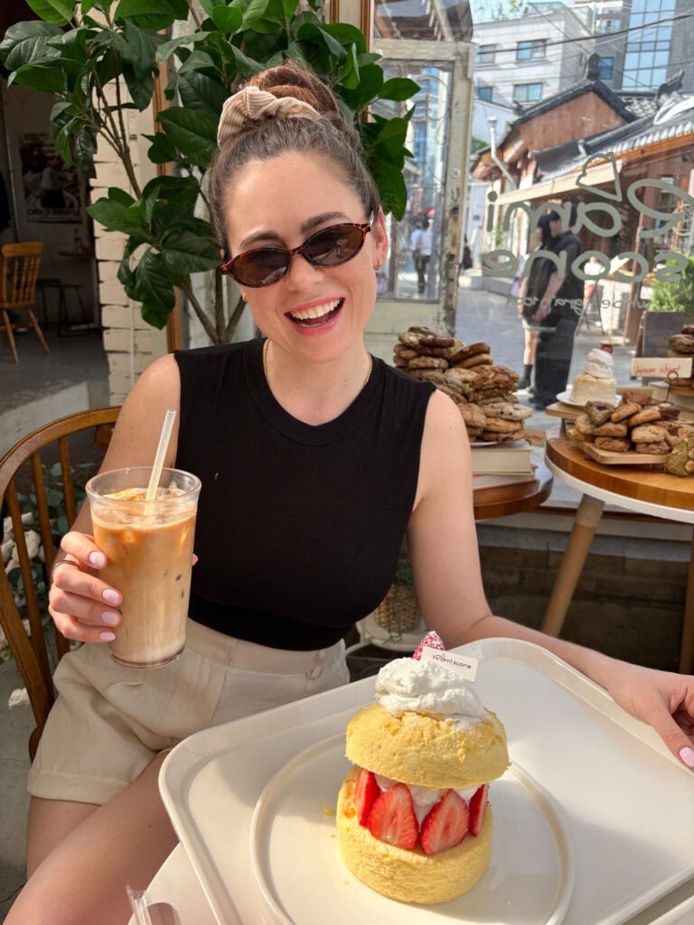 Sarah smiling with a coffee and strawberry souffle cake