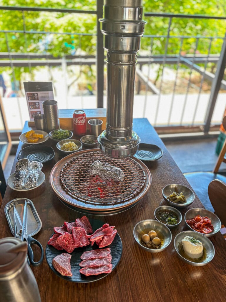 Korean barbecue table with meat and banchan and charcoal grill.