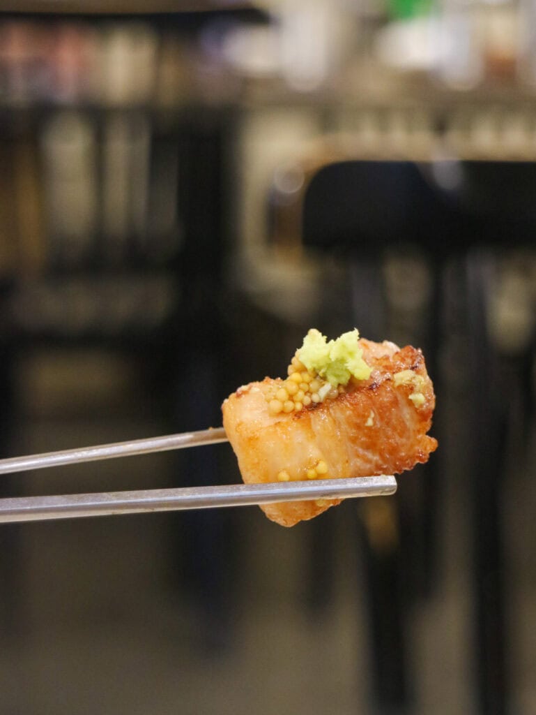 Chopsticks holding a piece of barbecued pork with wasabi