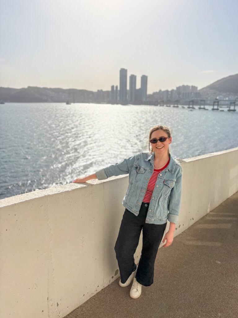 Smiling woman by the water with city skyline in the background.
