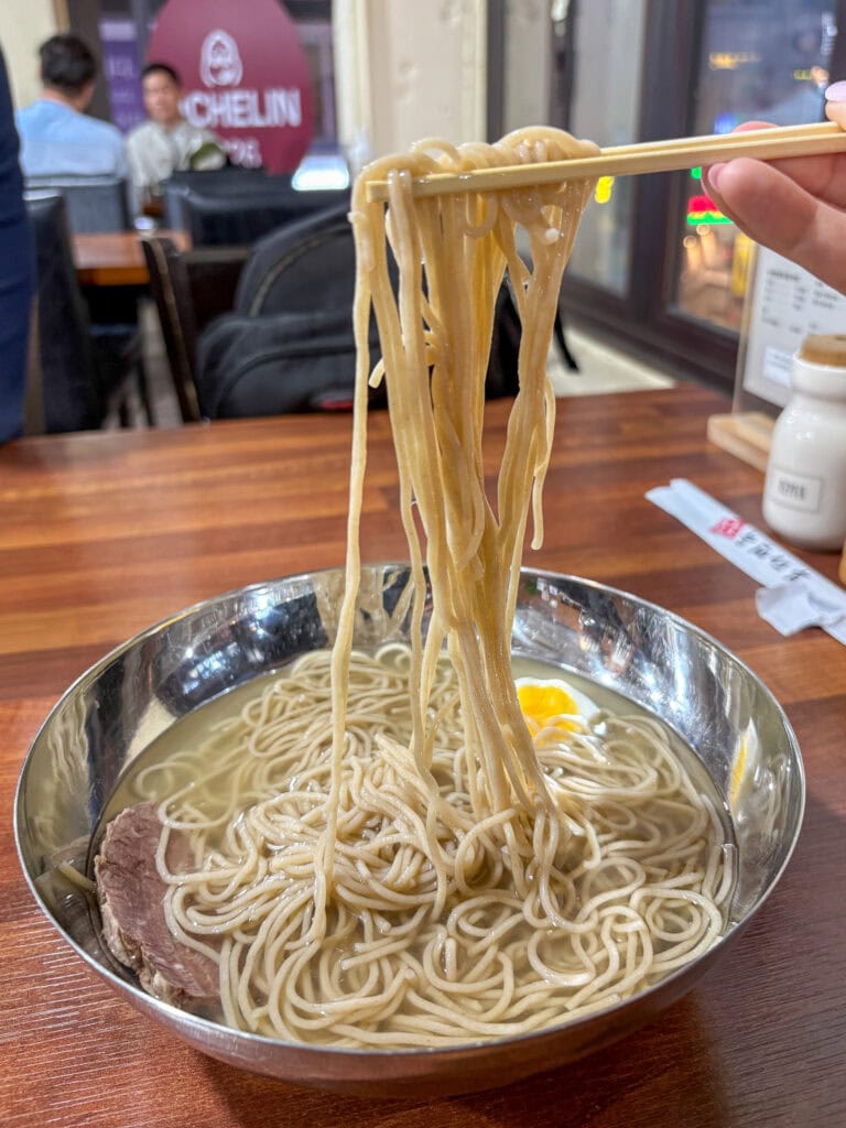 Bowl of steaming ramen noodles with chopsticks in a restaurant setting.
