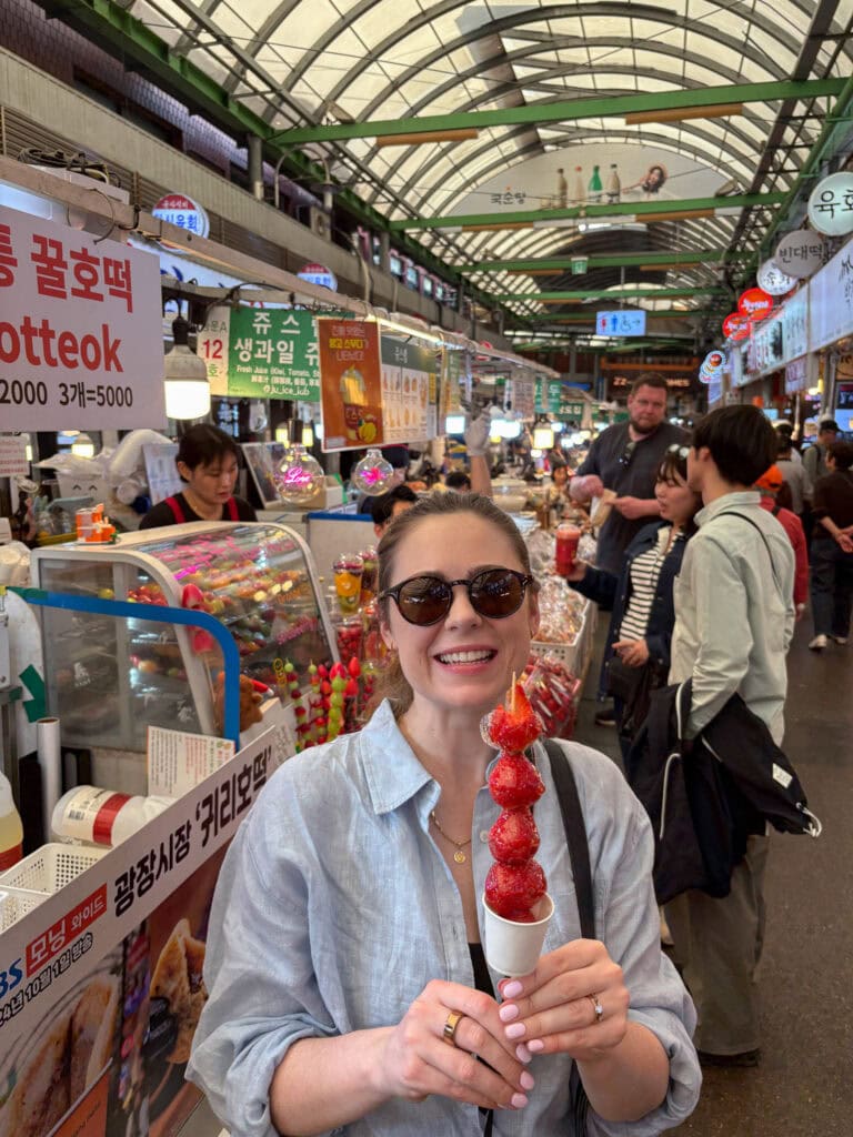 Woman enjoying Korean street food at a busy market in South Korea.