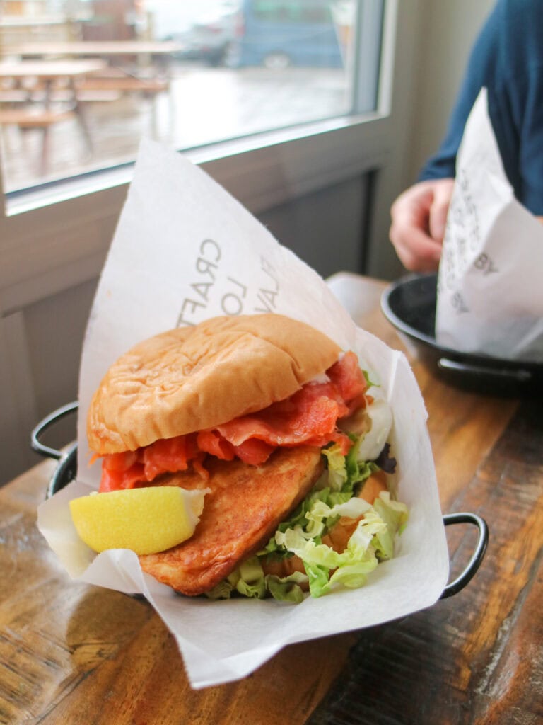 Delicious salmon sandwich with lettuce and lemon on a wooden table.
