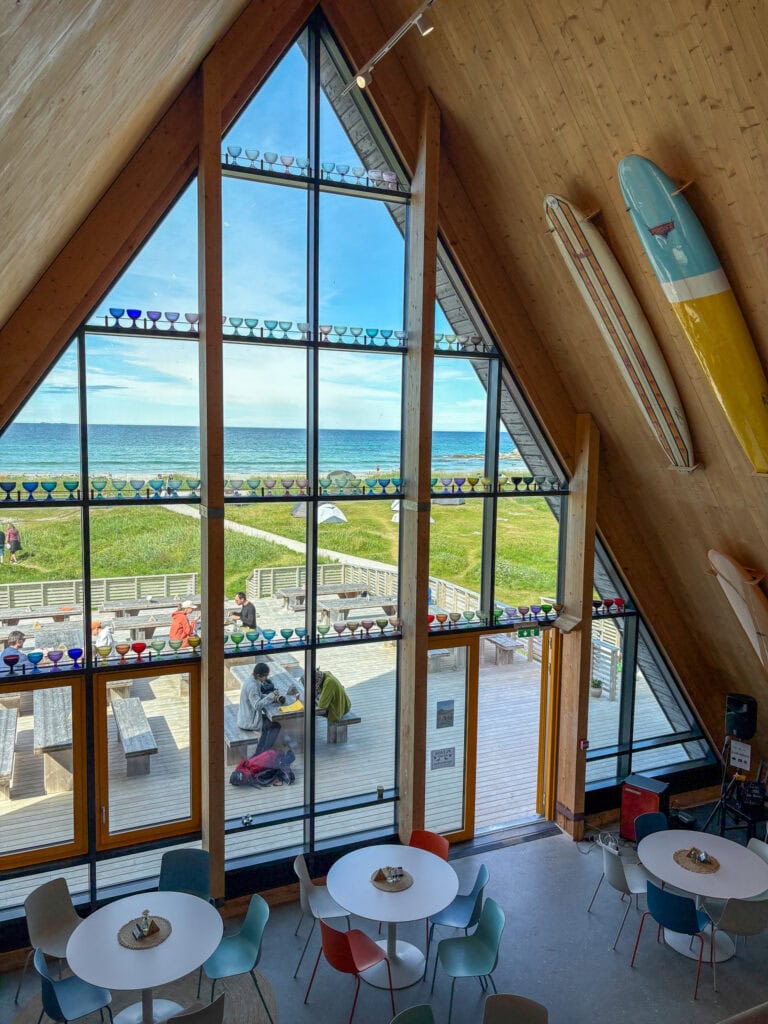 Interior view of a seaside cafe with large windows and surfboards on the wall.