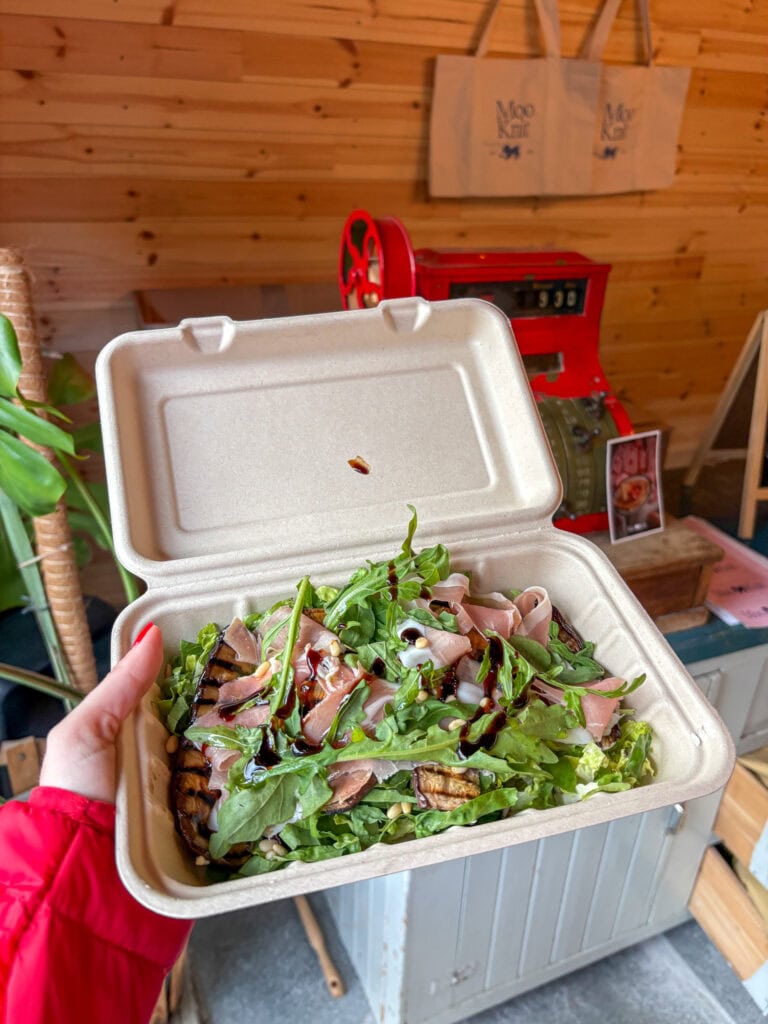 Fresh salad with greens and sliced meat in a takeout container at a rustic shop.