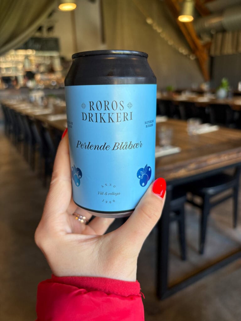 Hand holding a can of Roros Drikker Perlande Blåbær soda in a restaurant setting.