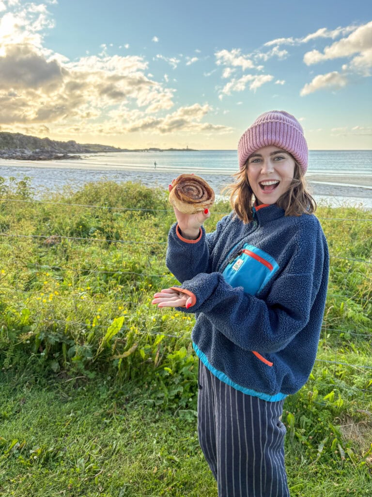 Woman enjoying a cinnamon roll at the beach during sunset.