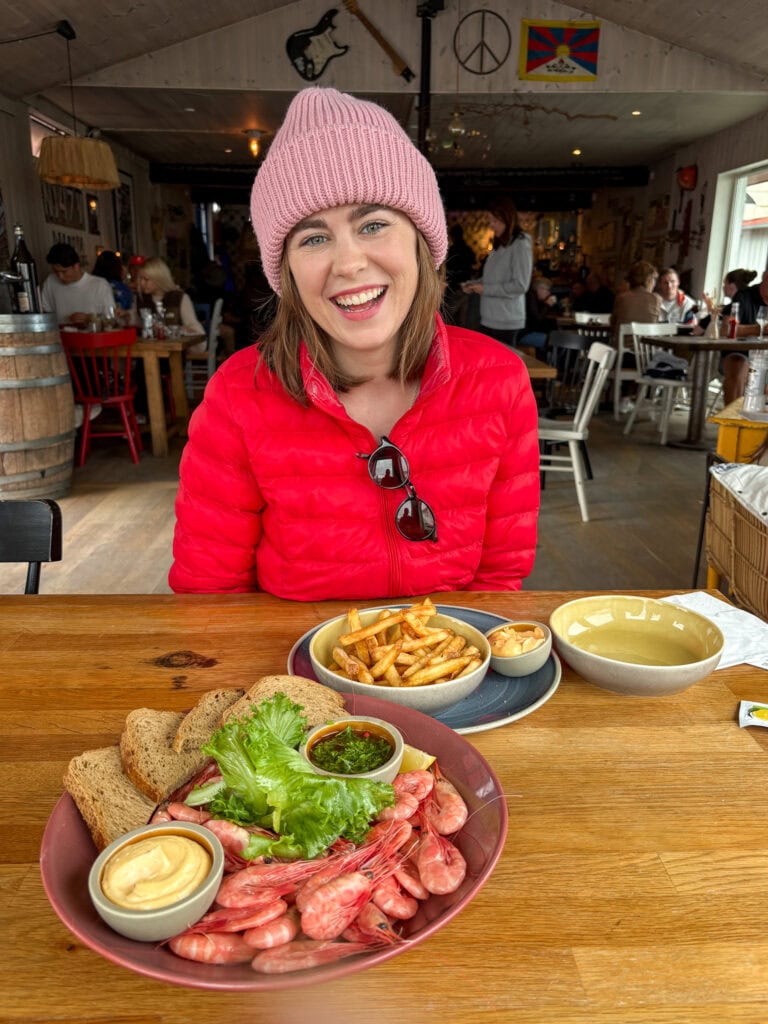 Smiling woman in pink hat and red jacket enjoying a meal at a cozy restaurant.