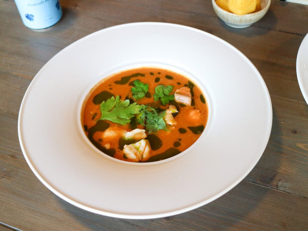 Delicious bowl of tomato-based soup with herbs and seafood garnishes.