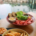 Seafood platter with shrimp, bread, and dipping sauces near a waterfront.