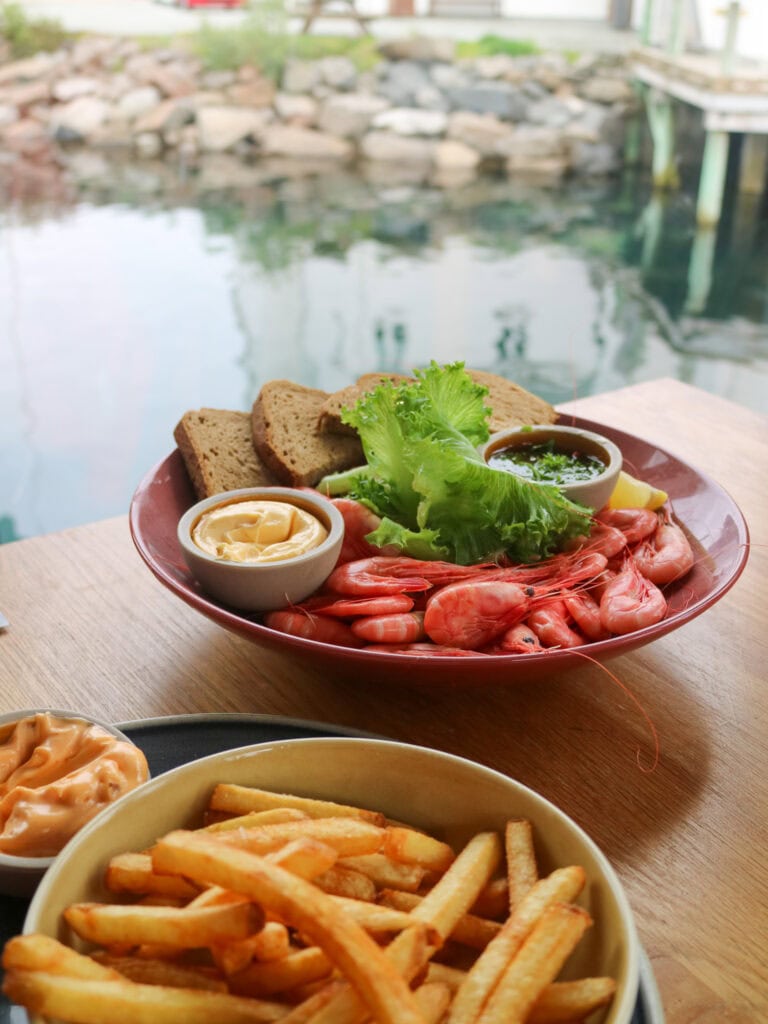 Seafood platter with shrimp, bread, and dipping sauces near a waterfront.