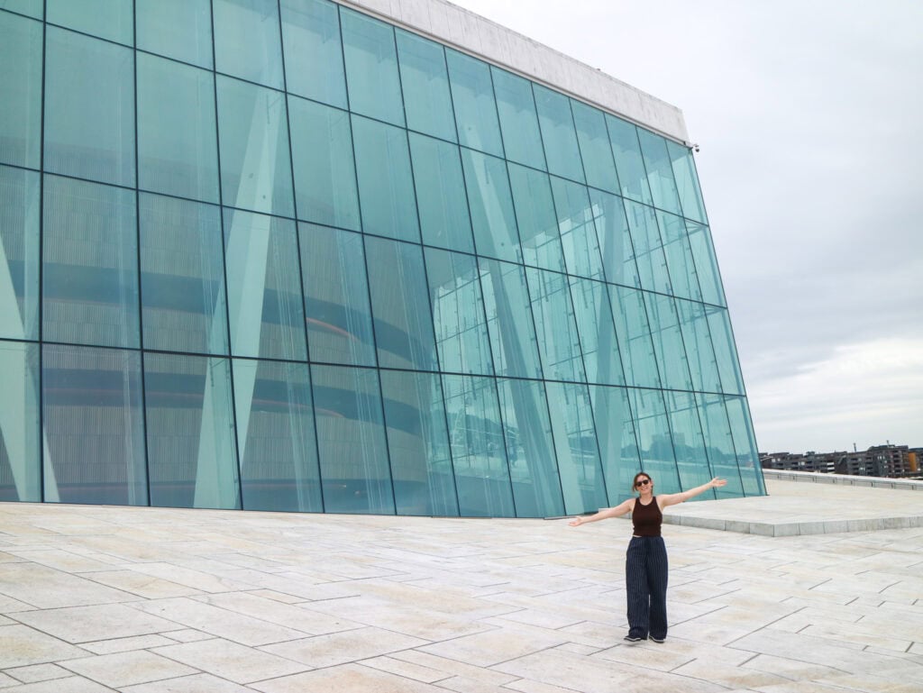 Woman standing outside modern glass building with arms outstretched.